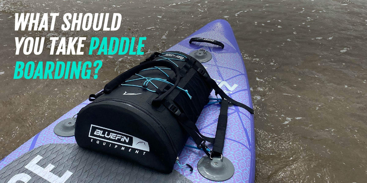 Lila Paddleboard mit schwarzer Ausrüstungstasche im flachen Wasser, mit Text zur Frage, was man zum Paddeln mitnimmt
