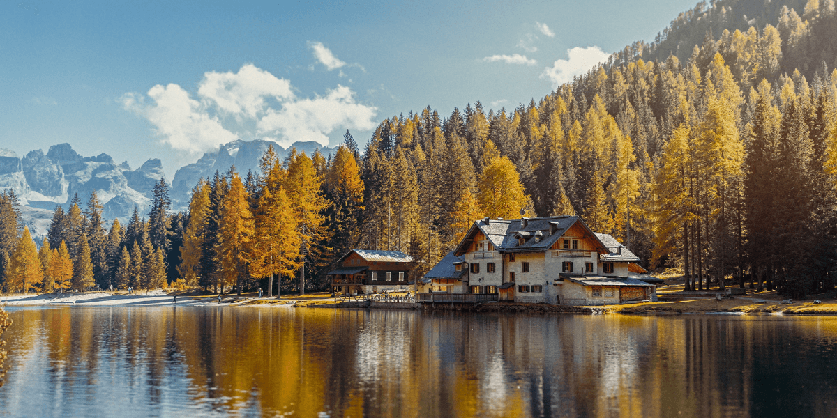Alpine lake reflecting an autumn forest and chalet, with rugged mountains in the background