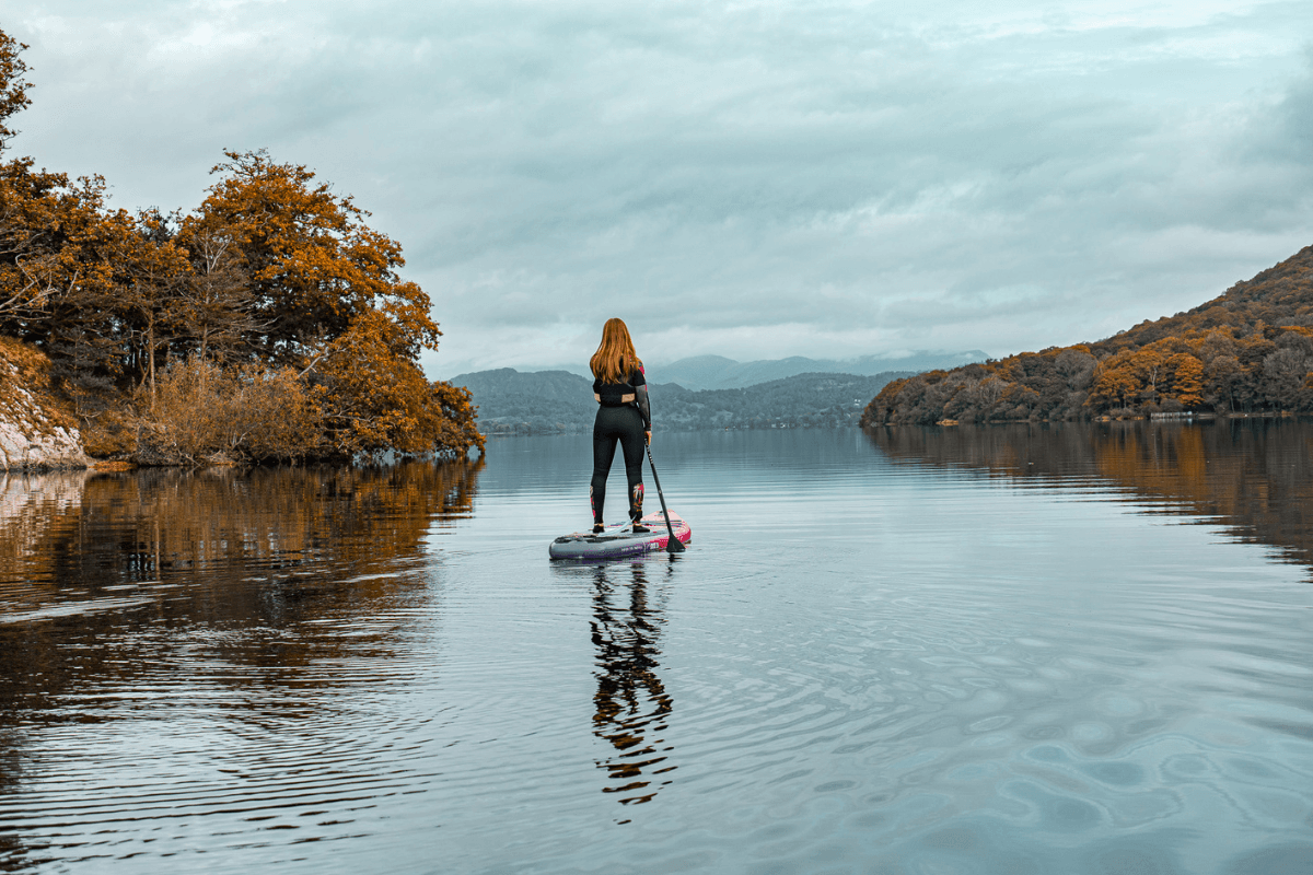 Donna mentre fa paddleboard su un lago autunnale
