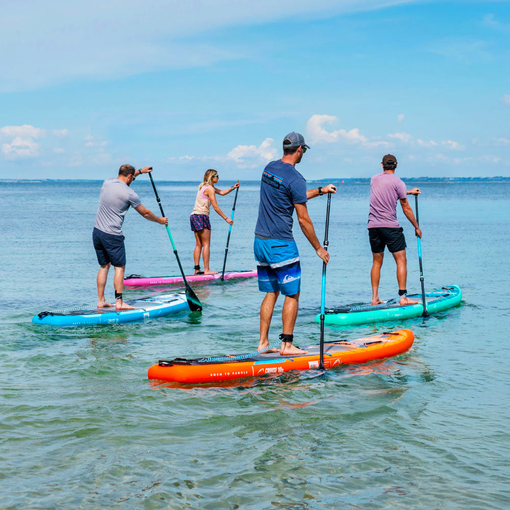 Four people paddleboarding on colorful boards in shallow water under a blue sky.