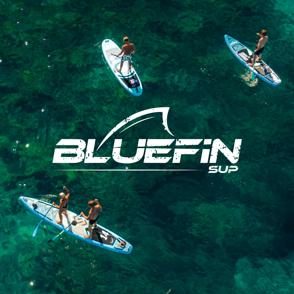 Two paddleboarders on blue inflatable boards in clear water, one paddling and one standing.