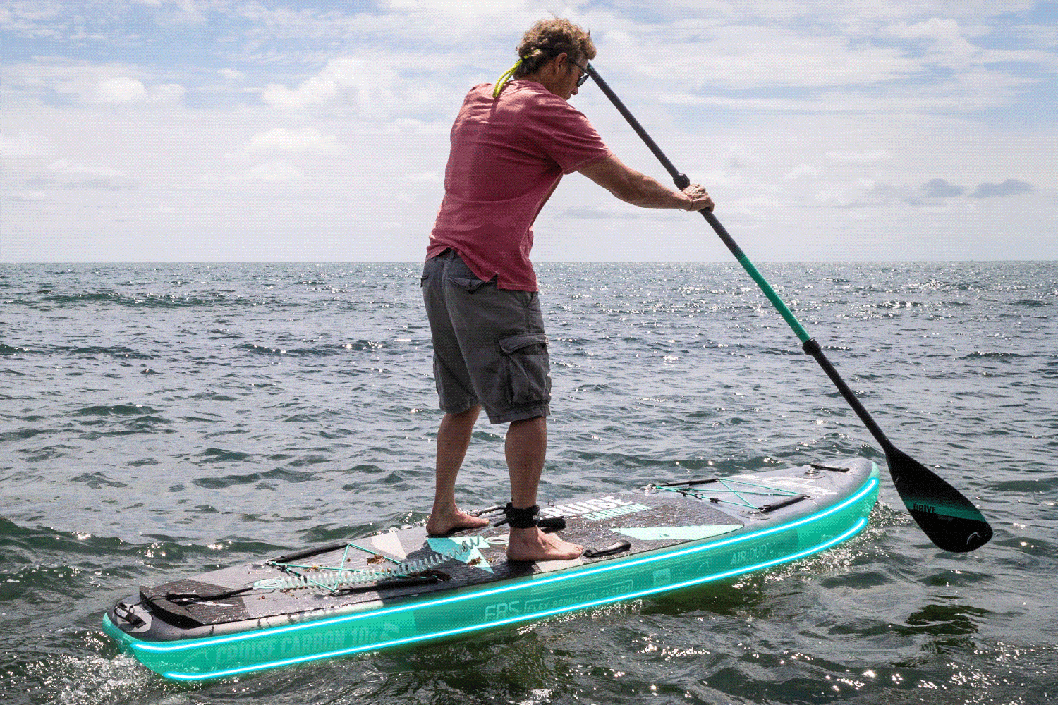 Person paddling on an inflatable paddleboard with a textured deck and green LED lights in the ocean