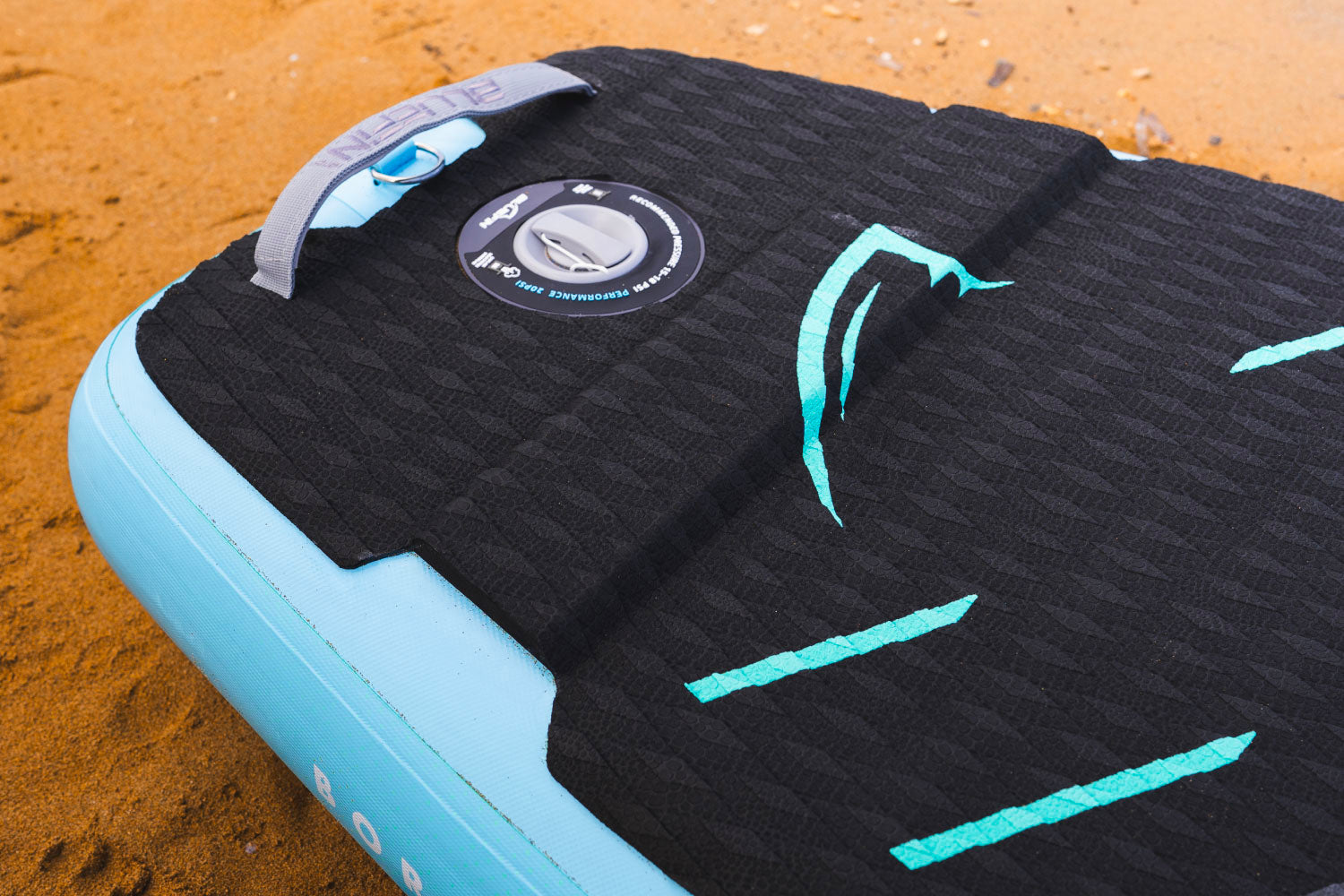 Inflatable paddleboard with textured black deck, center fin, and inflation valve on a sandy surface