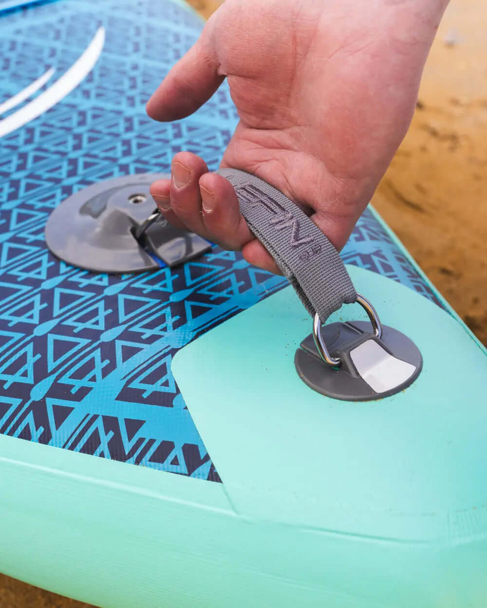 Hand gripping a gray strap on a blue and green inflatable paddleboard with a textured surface
