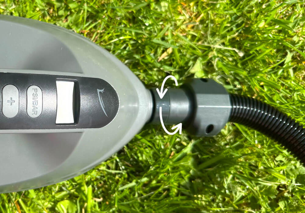 Close-up of a gray pump handle with buttons and a hose connector on green grass