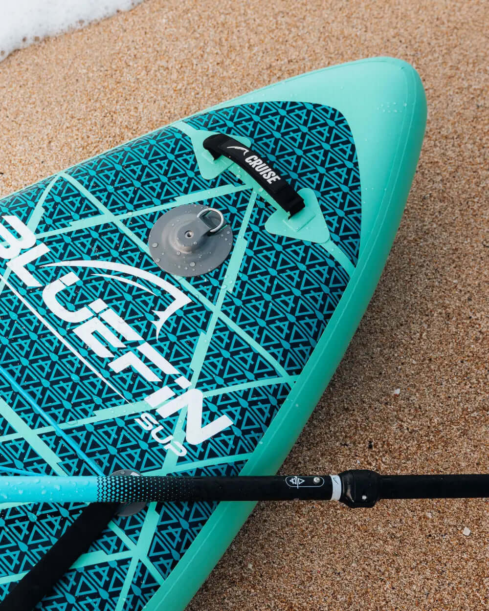 Inflatable paddleboard with geometric design, center fin, and inflation valve on sandy beach