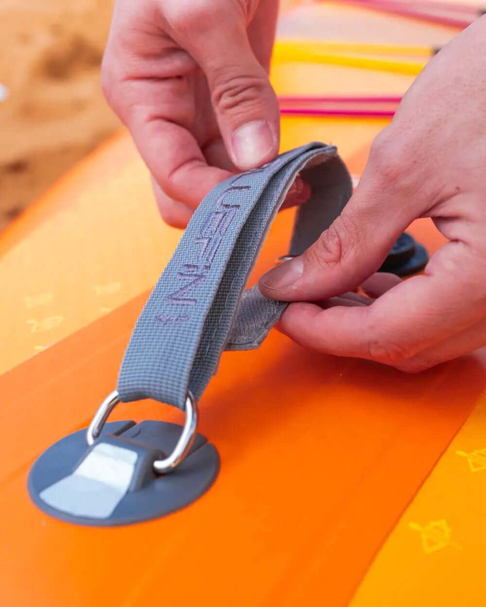 Hands adjusting a gray strap on an orange inflatable paddleboard with a fin and valve