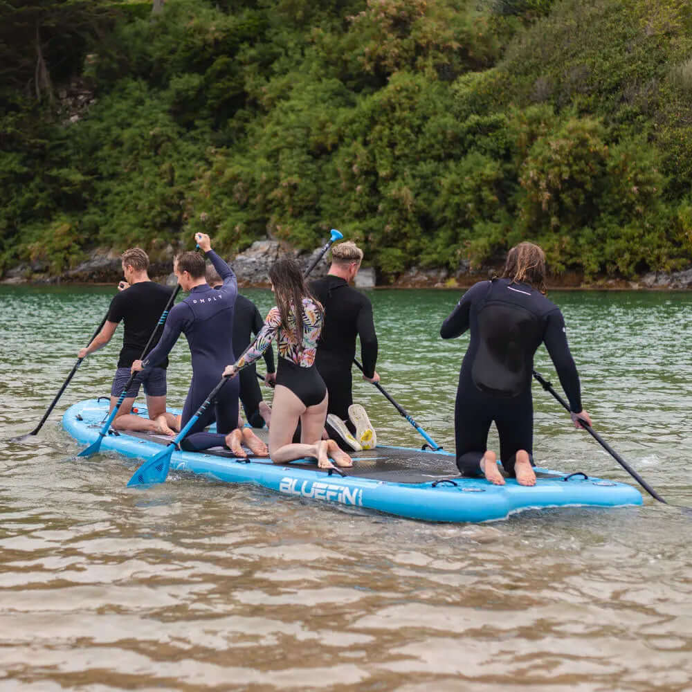 Gruppe von sechs Personen, die auf einem blauen aufblasbaren Paddleboard in ruhigem Wasser paddeln