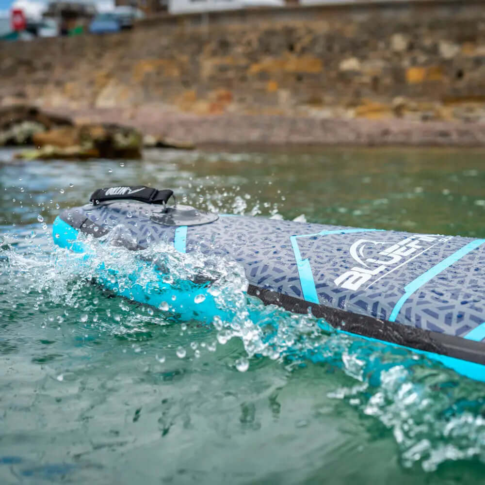 Paddleboard inflable con superficie texturizada, acentos azules y agua salpicando a su alrededor