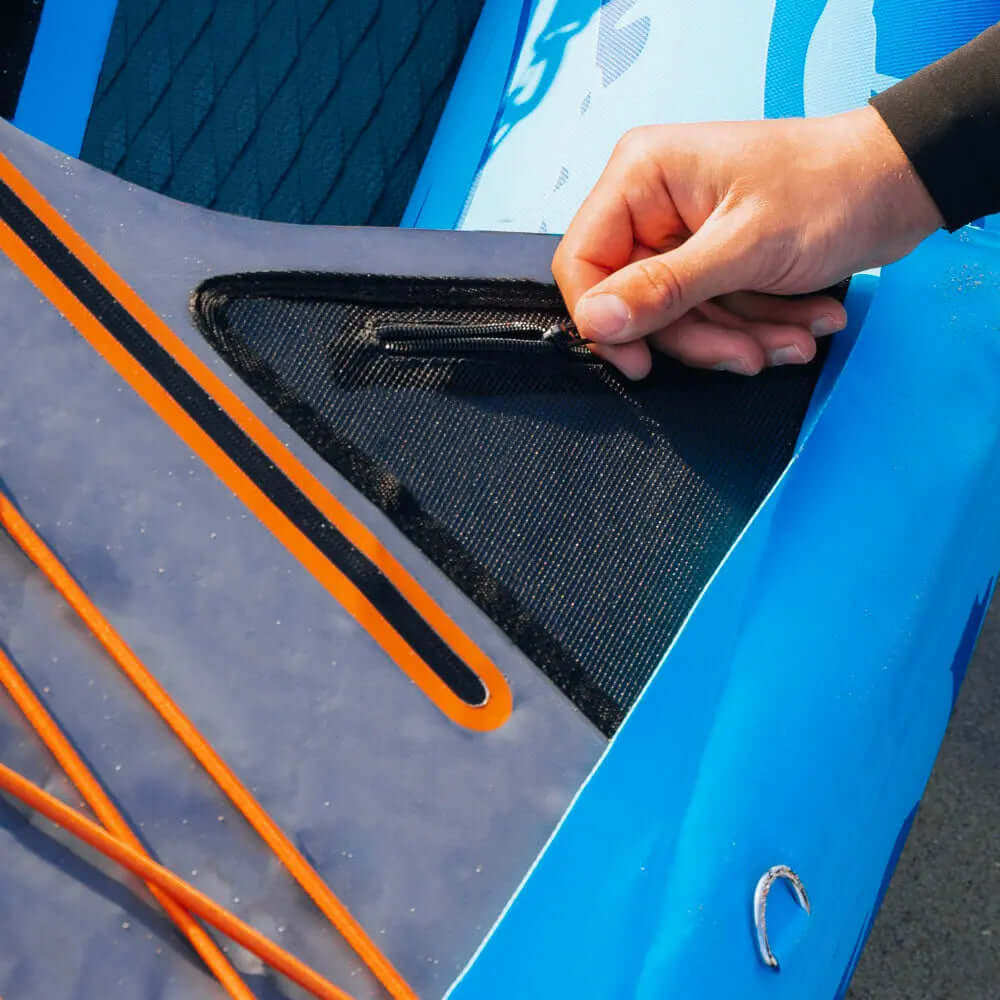 Hand adjusting the zipper on a paddleboard's storage compartment with orange bungee cords visible