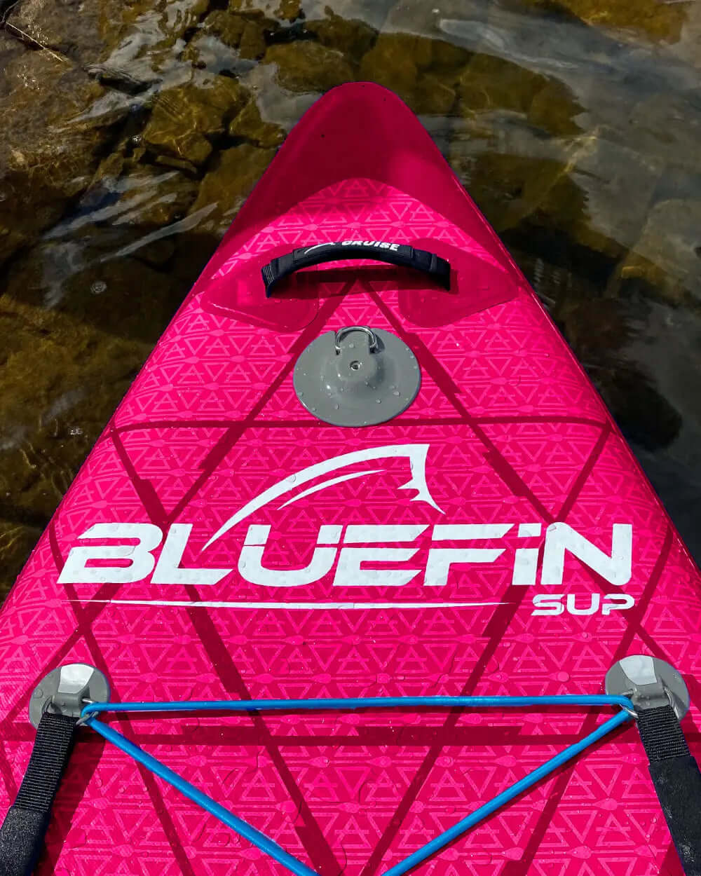 Pink inflatable paddleboard with textured surface, center fin, and bungee cord for gear storage