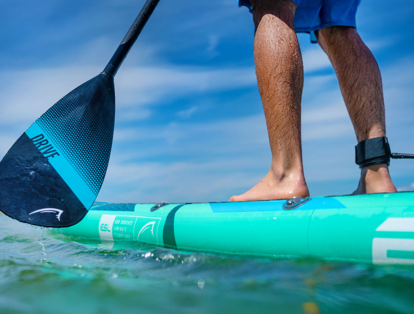 Person standing on a turquoise paddleboard with a black paddle in clear water