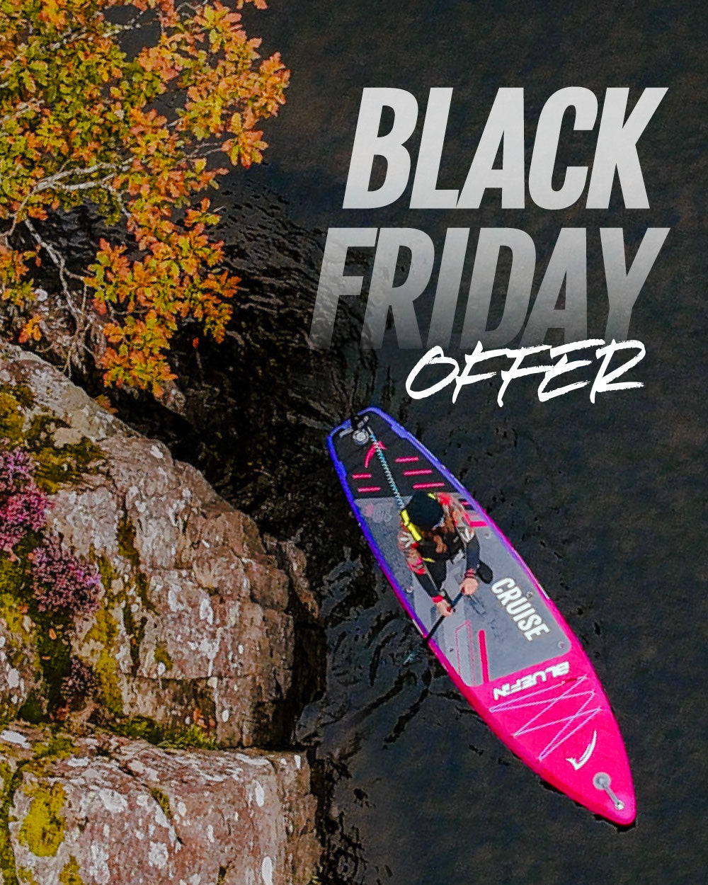 Inflatable paddleboard in pink and gray on water near rocky shore with autumn foliage