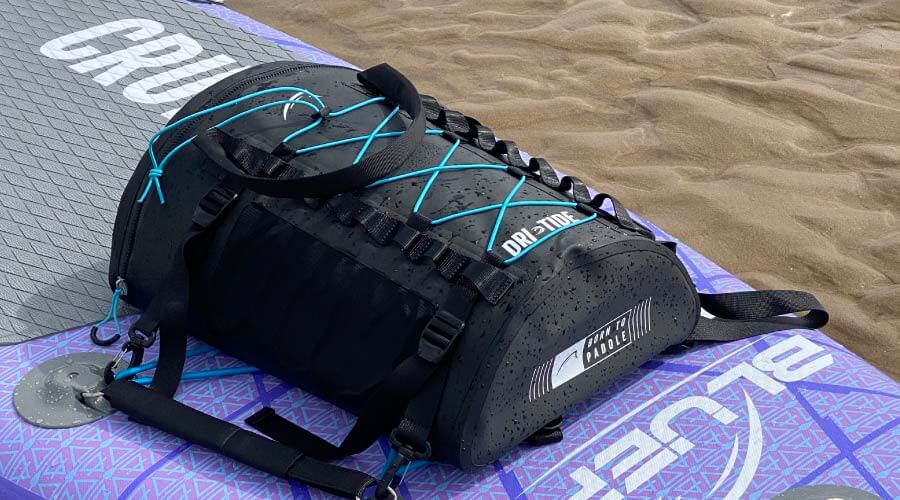 Water-resistant black duffel bag with blue accents on a paddleboard on sandy beach