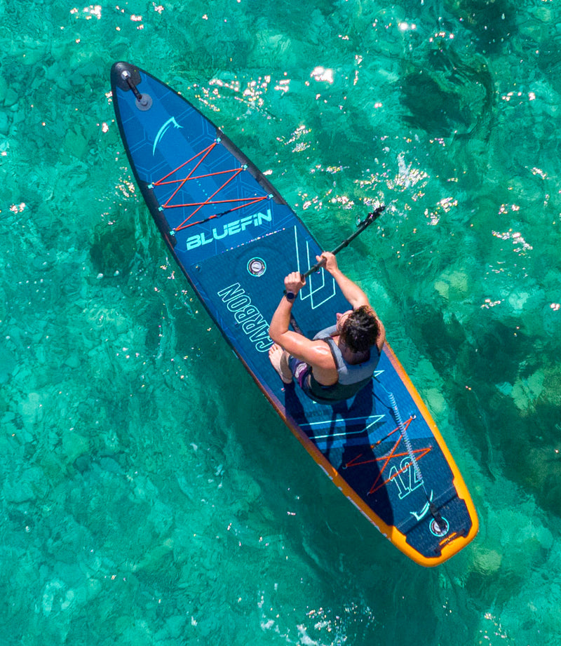 Person paddling a blue inflatable paddleboard on clear turquoise water