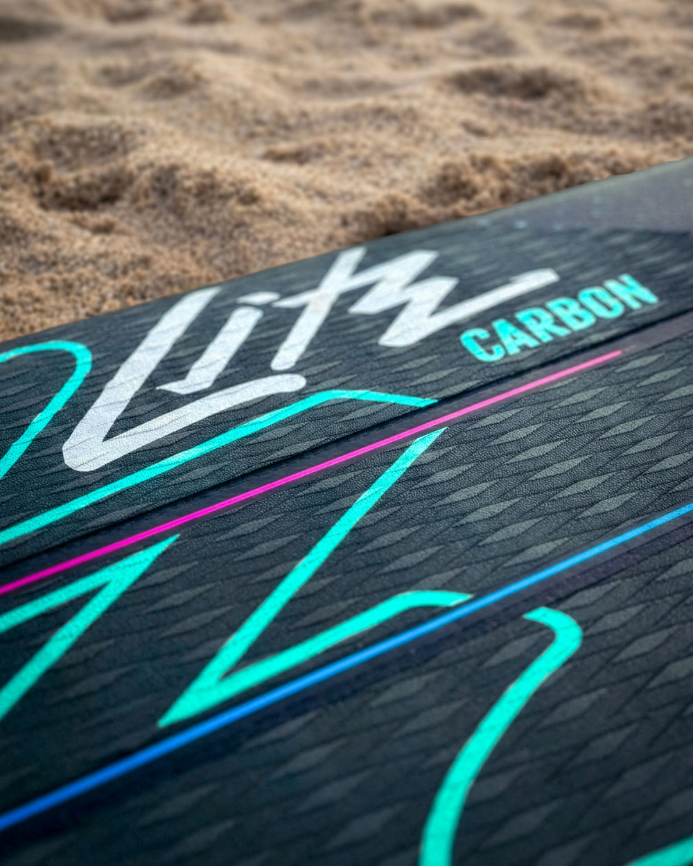 Close-up of a black paddleboard deck with colorful graphics and the word 'Carbon' in blue.