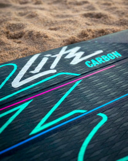 Close-up of a black paddleboard deck with colorful graphics and the word 'Carbon' in blue.