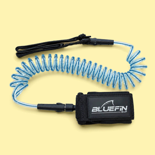 Coiled blue SUP leash with black ankle strap and Bluefin logo on the cuff.