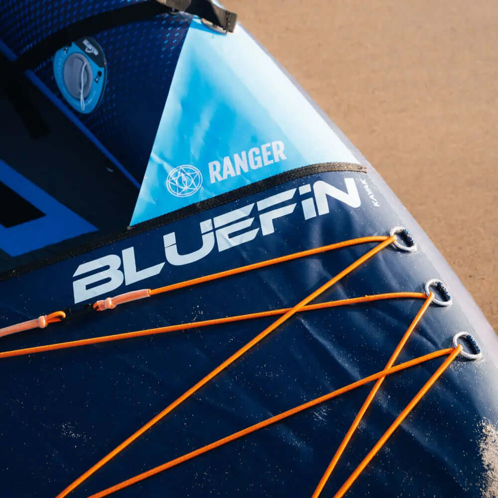 Aufblasbares Paddleboard mit blauem und marineblauem Design, mit dem Namen Bluefin und orangefarbenen Bungee-Kordeln.