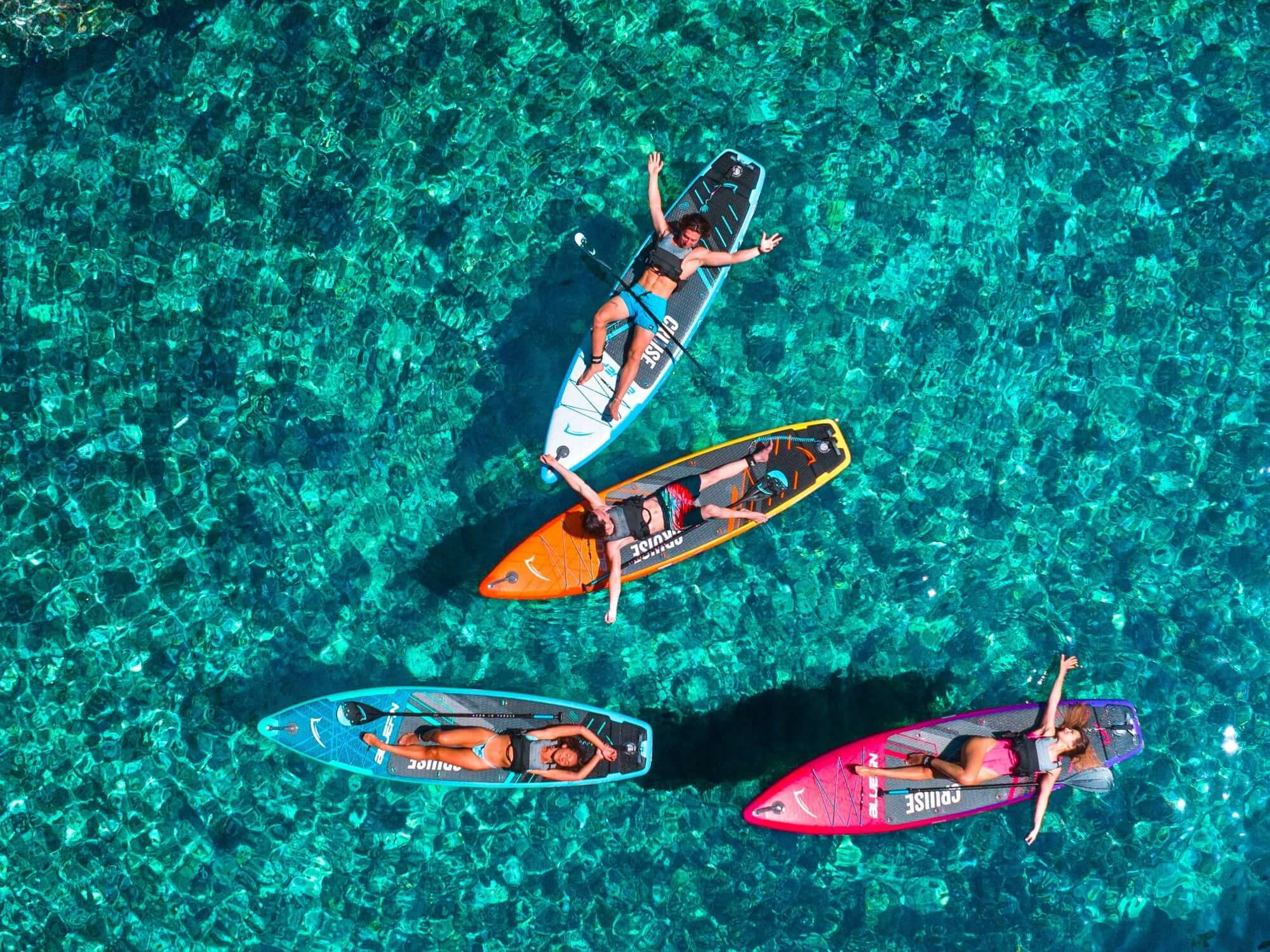 Quatre paddleboarders se détendent sur des planches colorées au-dessus d'une eau turquoise claire